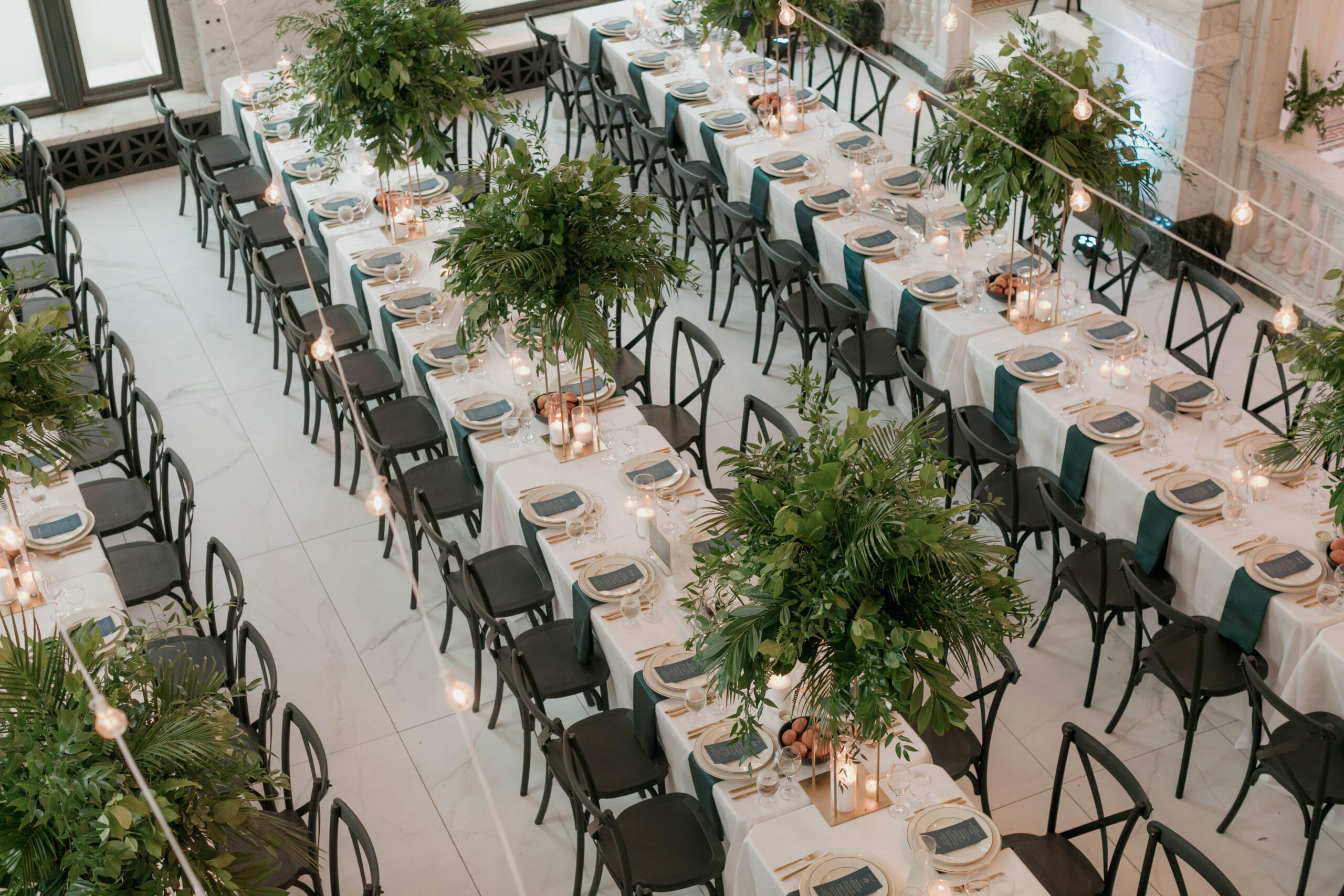 above view of long tables, with 15 chairs on each side, featuring tall greenery arrangements and low candle votives